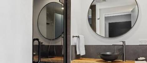 Une salle de bain moderne avec une douche à parois de verre, un miroir rond et un meuble-lavabo en bois.