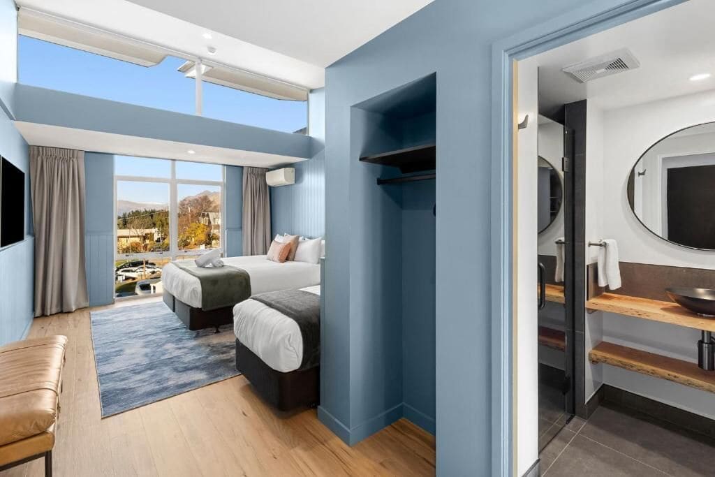 A modern hotel room with a large bed, a desk, and a view of a mountainous landscape.