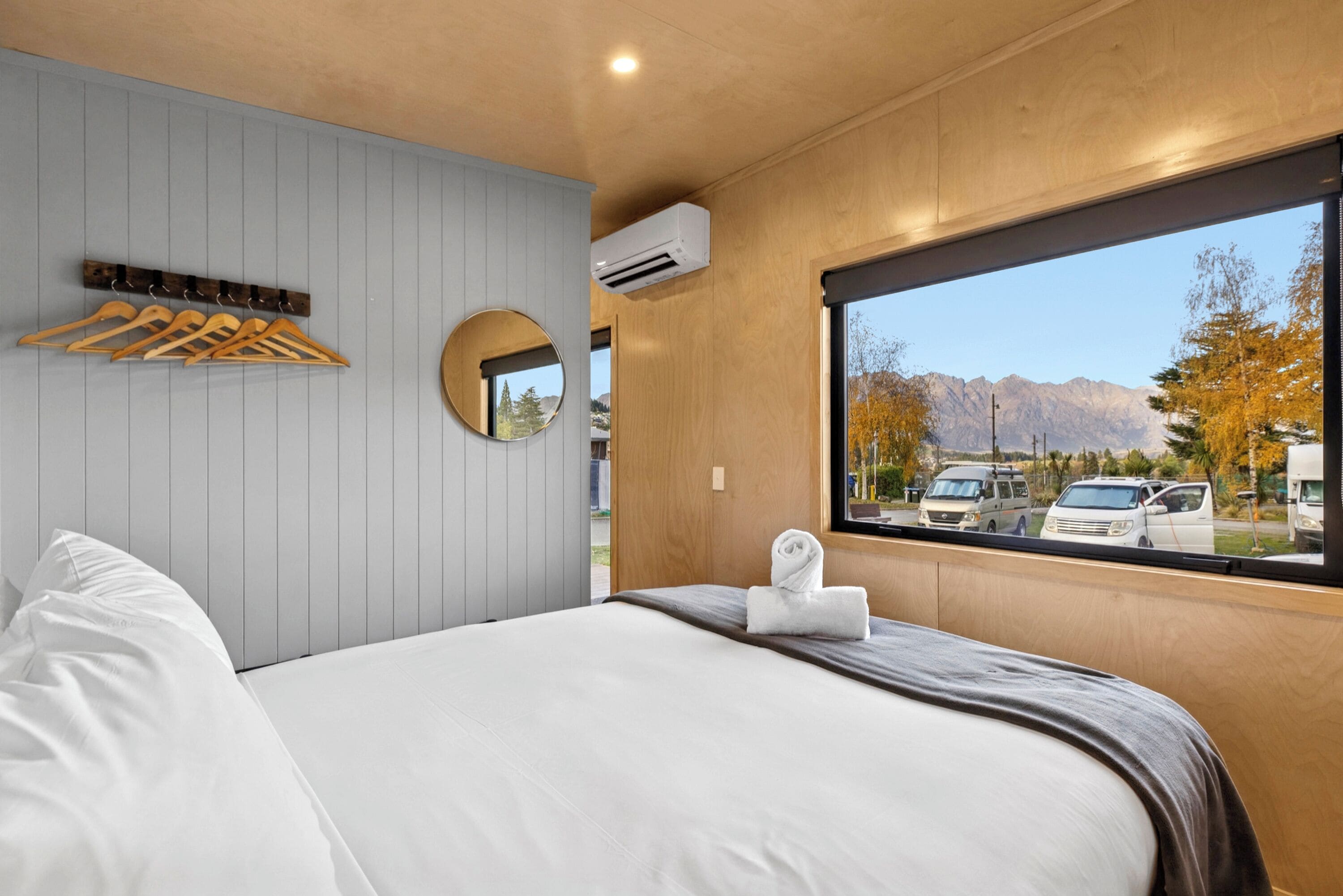 Una habitación de hotel con cama, ventana con vistas a la montaña, espejo y unidad de aire acondicionado.