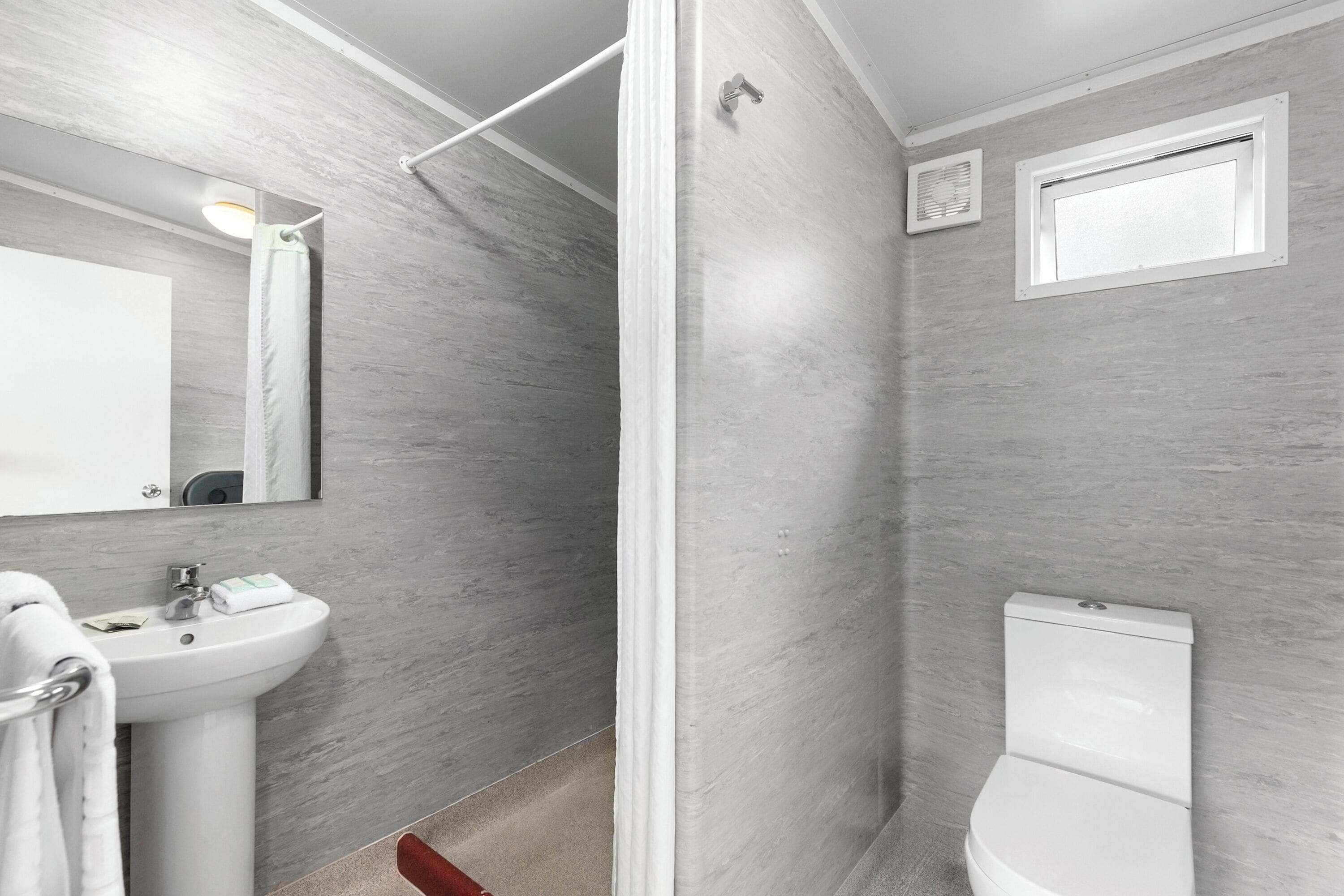 A modern bathroom with a pedestal sink, a toilet, and a shower area.