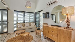 A modern living room with a sofa, two round tables, a wooden cabinet, a large mirror, and a ceiling light. - Julians Apartments (Byron Bay)