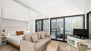 A modern bedroom with a bed, sofa, TV, and large windows. - Julians Apartments (Byron Bay)