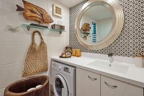 Ein kleines Badezimmer mit Waschmaschine, Waschbecken, Spiegel und dekorativen Gegenständen auf Regalen.