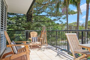 Ein Balkon mit Holzstühlen und einem Tisch, umgeben von einem Metallgeländer, mit Blick auf eine üppige grüne Landschaft.