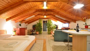 A cozy attic bedroom with a sloped wooden ceiling, a bed, a desk, a chair, and potted plants.