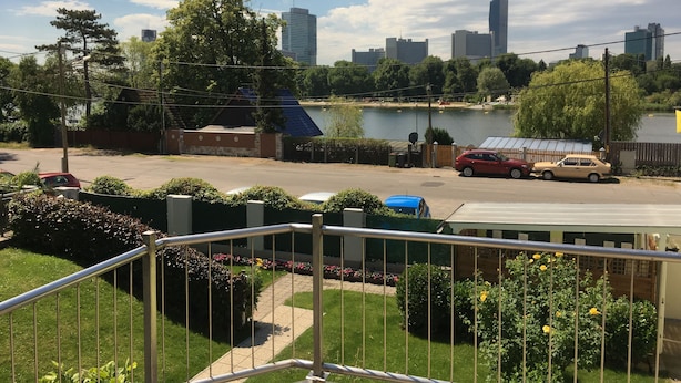 A residential area with a view of a lake, a city skyline, and a gated entrance with a blue car parked inside.