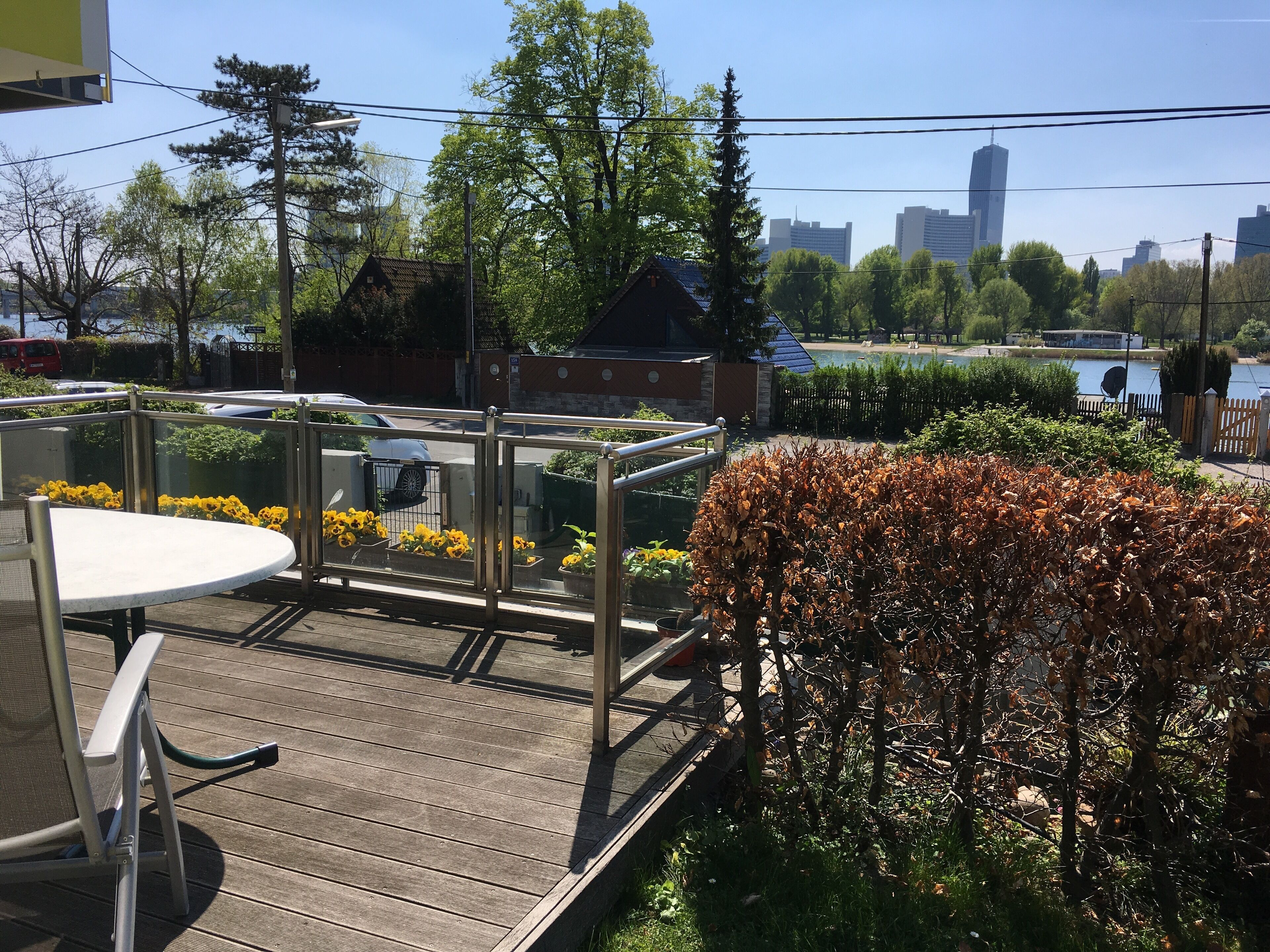 A wooden deck with a table and chairs, surrounded by potted plants and a metal railing.