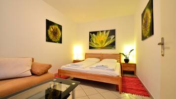 A bedroom with a bed, bedside tables, a nightstand, a red rug, and a glass table with a chair.