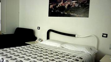 A hotel room with a bed, a nightstand, a telephone, and a painting of a town on the wall.
