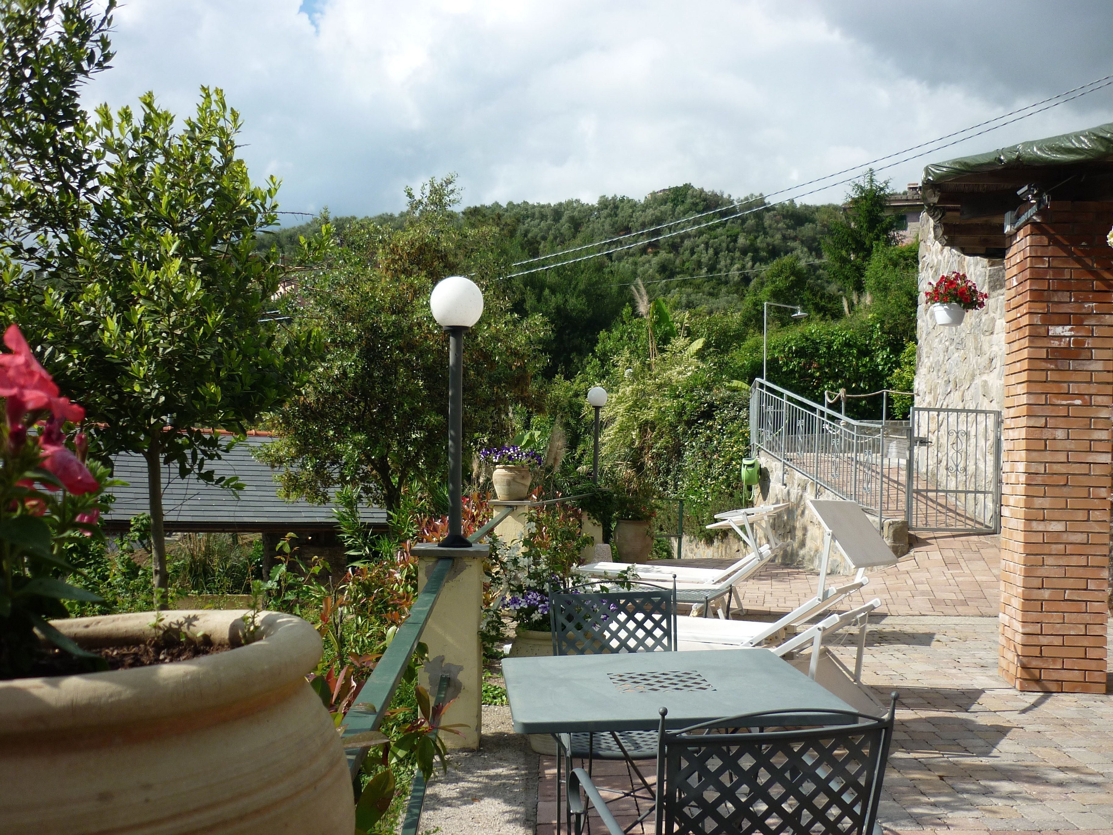 A patio with a table and chairs, surrounded by potted plants and a view of a hillside.