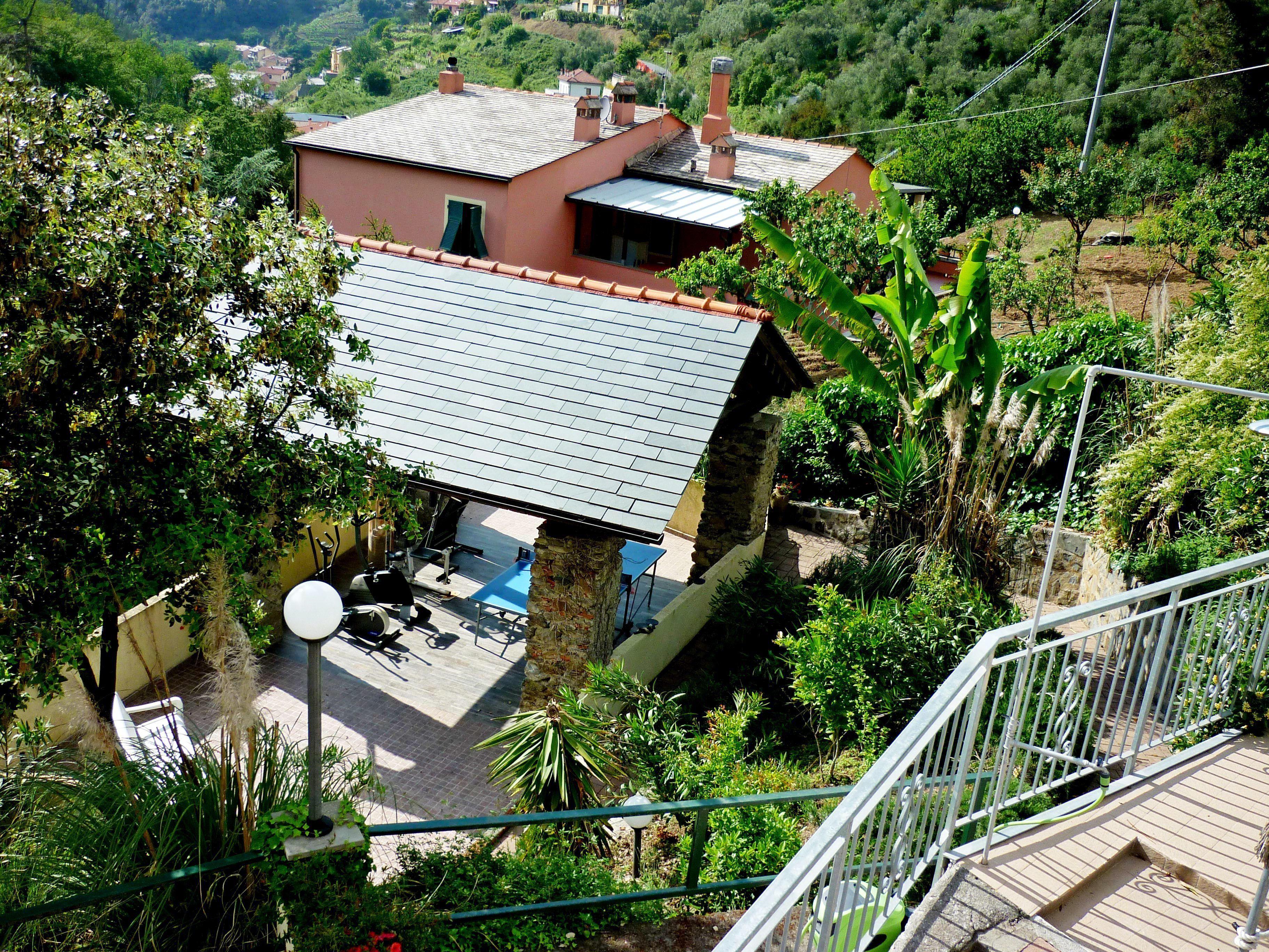 A house with a sloped roof, surrounded by lush greenery and a view of a hilly landscape.