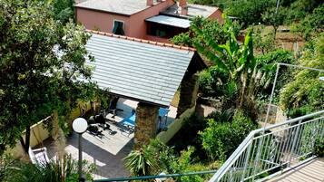 A house with a sloped roof, surrounded by lush greenery and a view of a hilly landscape.