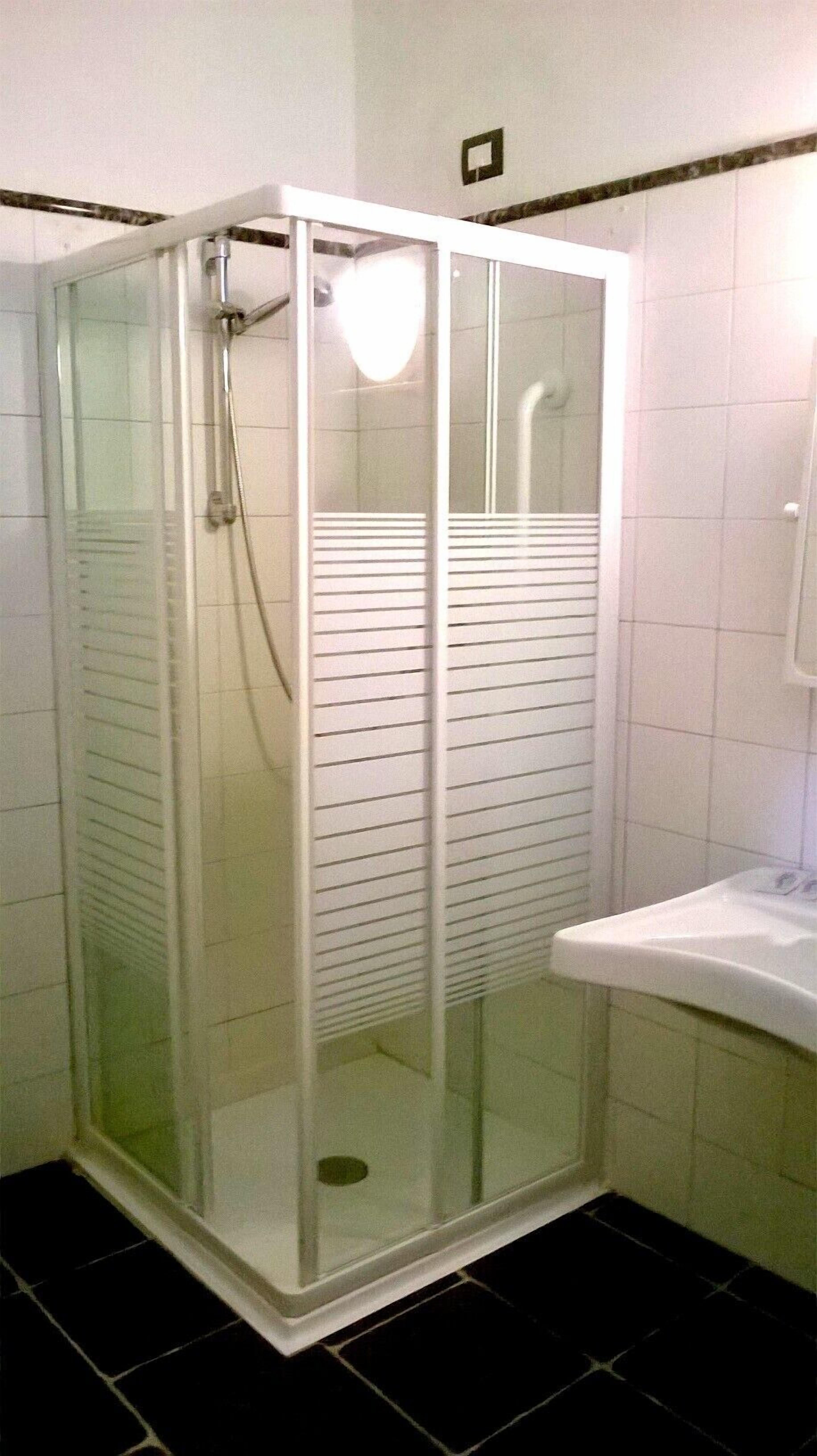 A glass-enclosed shower stall with a white sink and tiled floor.