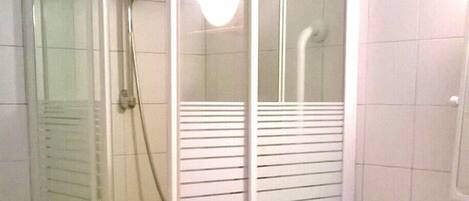 A glass-enclosed shower stall with a white sink and tiled floor.