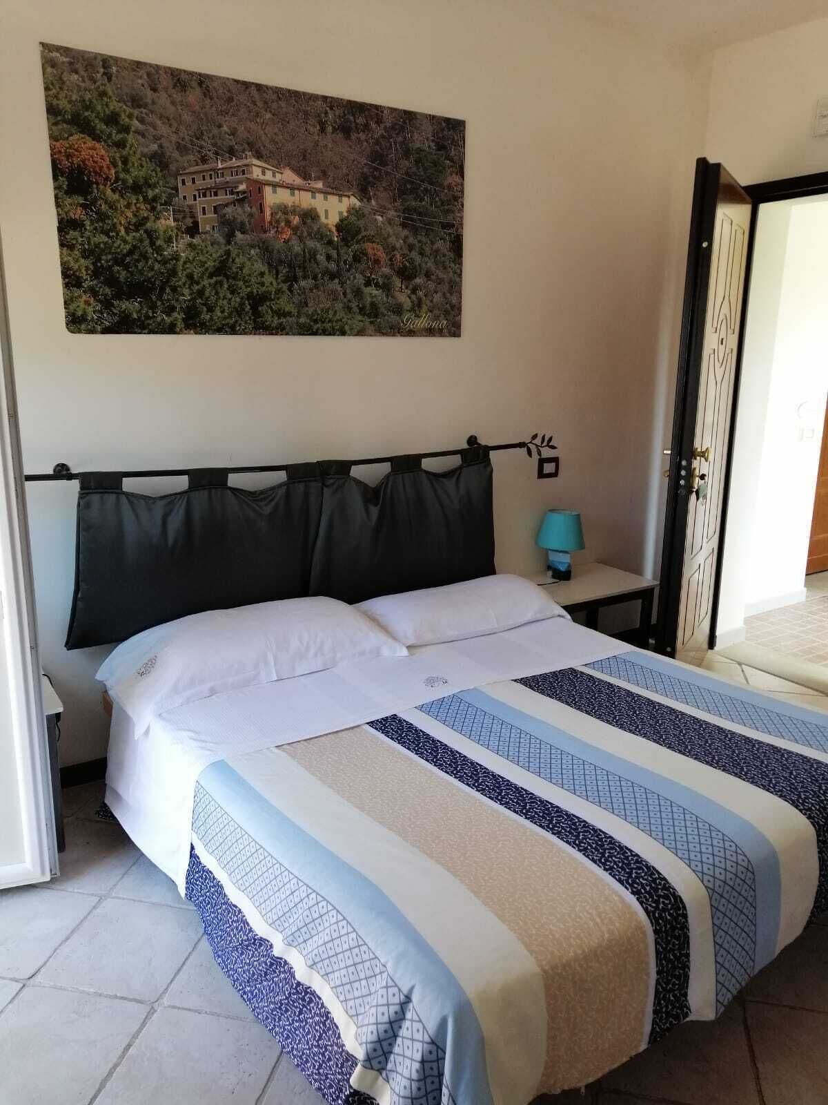 Een slaapkamer met een bed, nachtkastje, lamp en schilderij aan de muur.