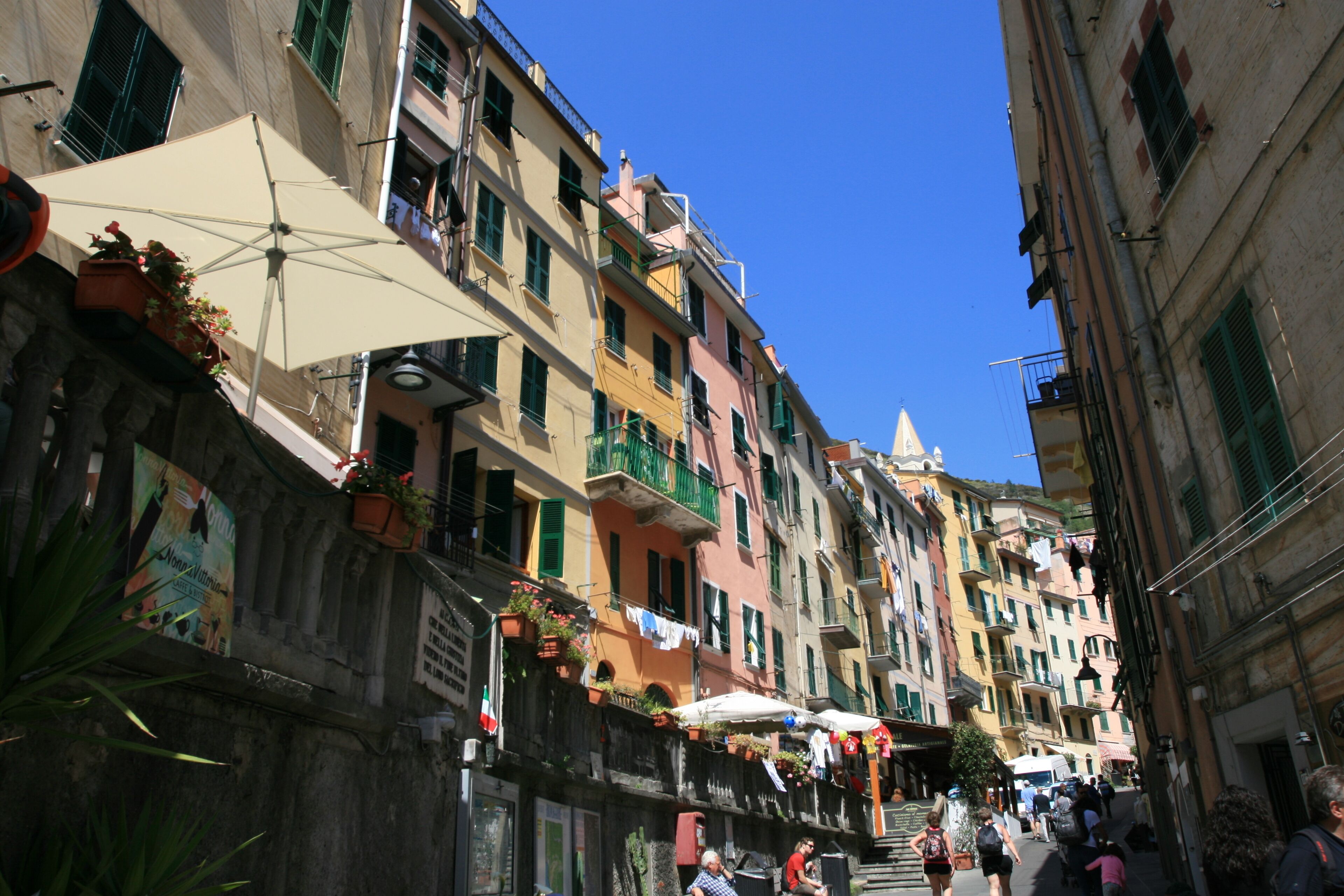 A narrow street lined with colorful buildings, some with balconies and potted plants.