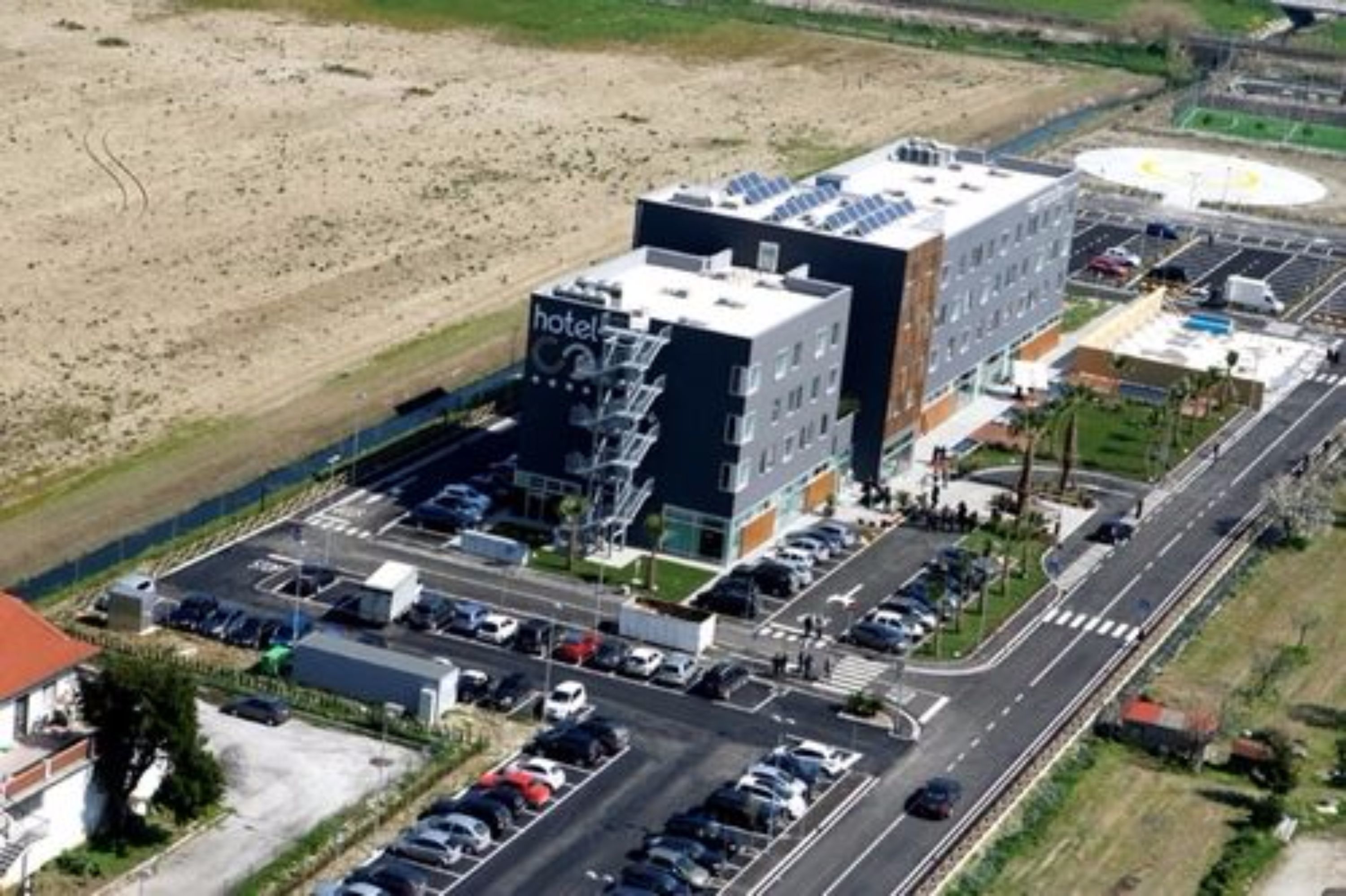A modern hotel with a rooftop solar panel installation, a parking lot, and a road intersection.