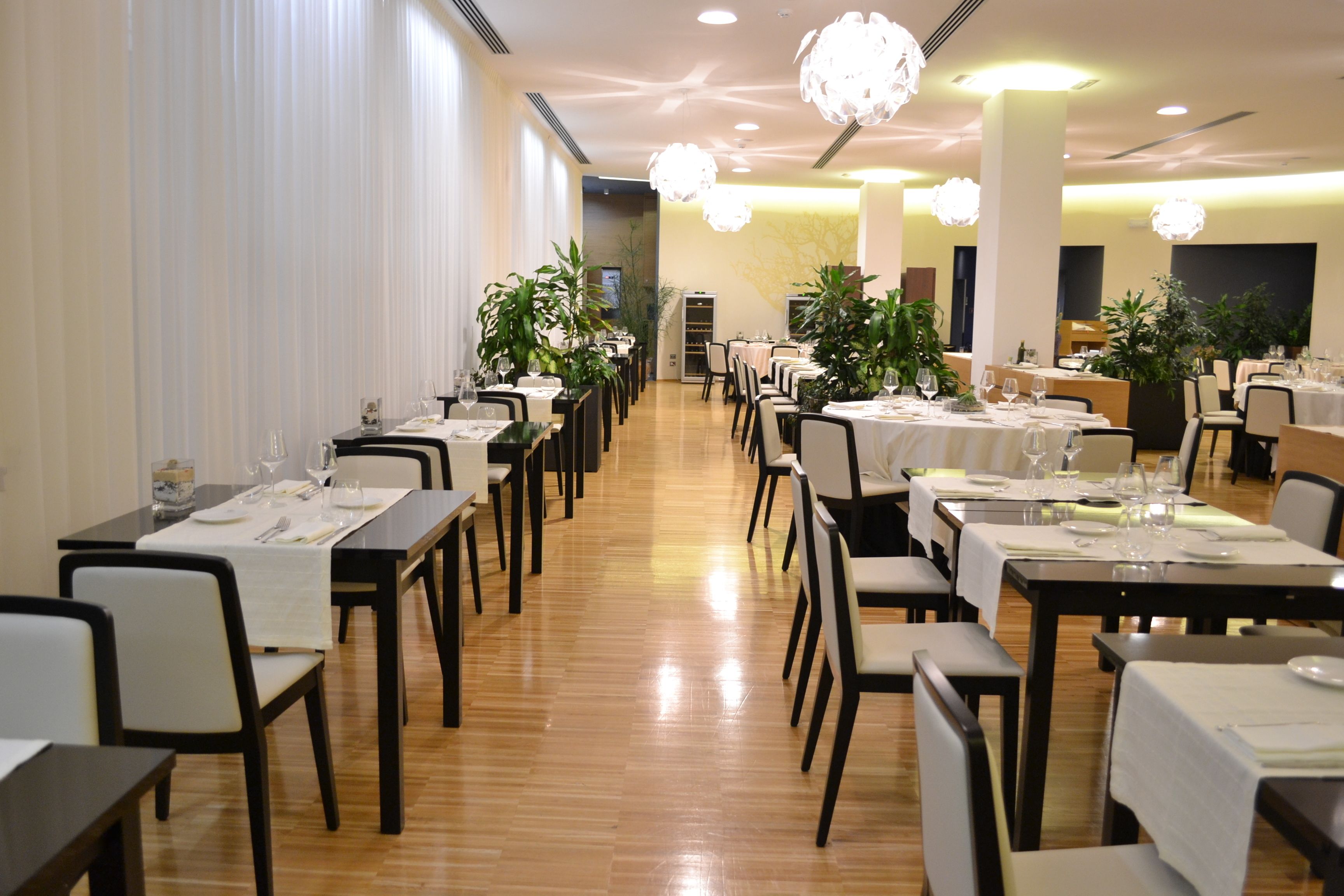A restaurant with long tables, chairs, and potted plants.