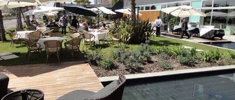 An outdoor pool area with lounge chairs and umbrellas, surrounded by a landscaped garden and a building with large windows.