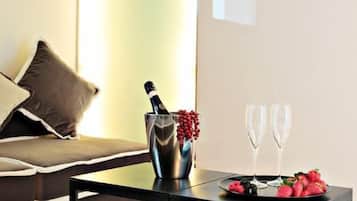 A modern living room with a sofa, a coffee table with a bottle and glasses, and a decorative plant on the wall.