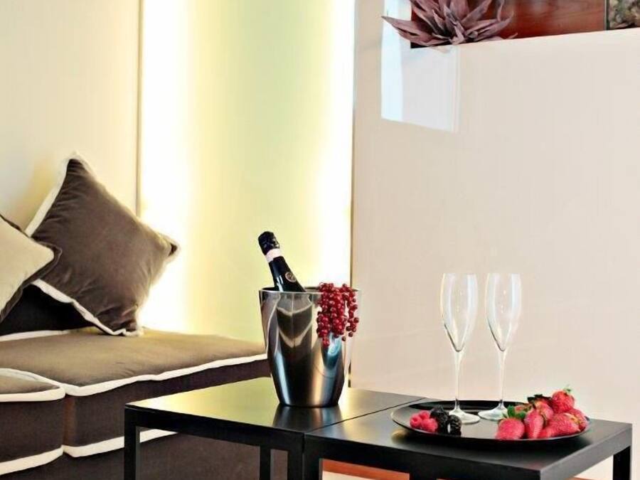 A modern living room with a sofa, a coffee table with a bottle and glasses, and a decorative plant on the wall.