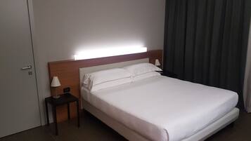 Ein Hotelzimmer mit einem großen Bett, einem Nachttisch mit Lampe, einer Tür und einem Vorhang.