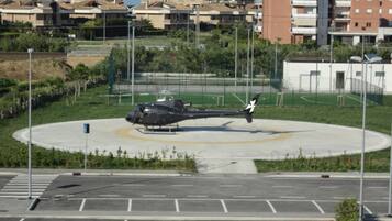 Un elicottero su un piazzale d'atterraggio, circondato da un'area di parcheggio e con edifici sullo sfondo.
