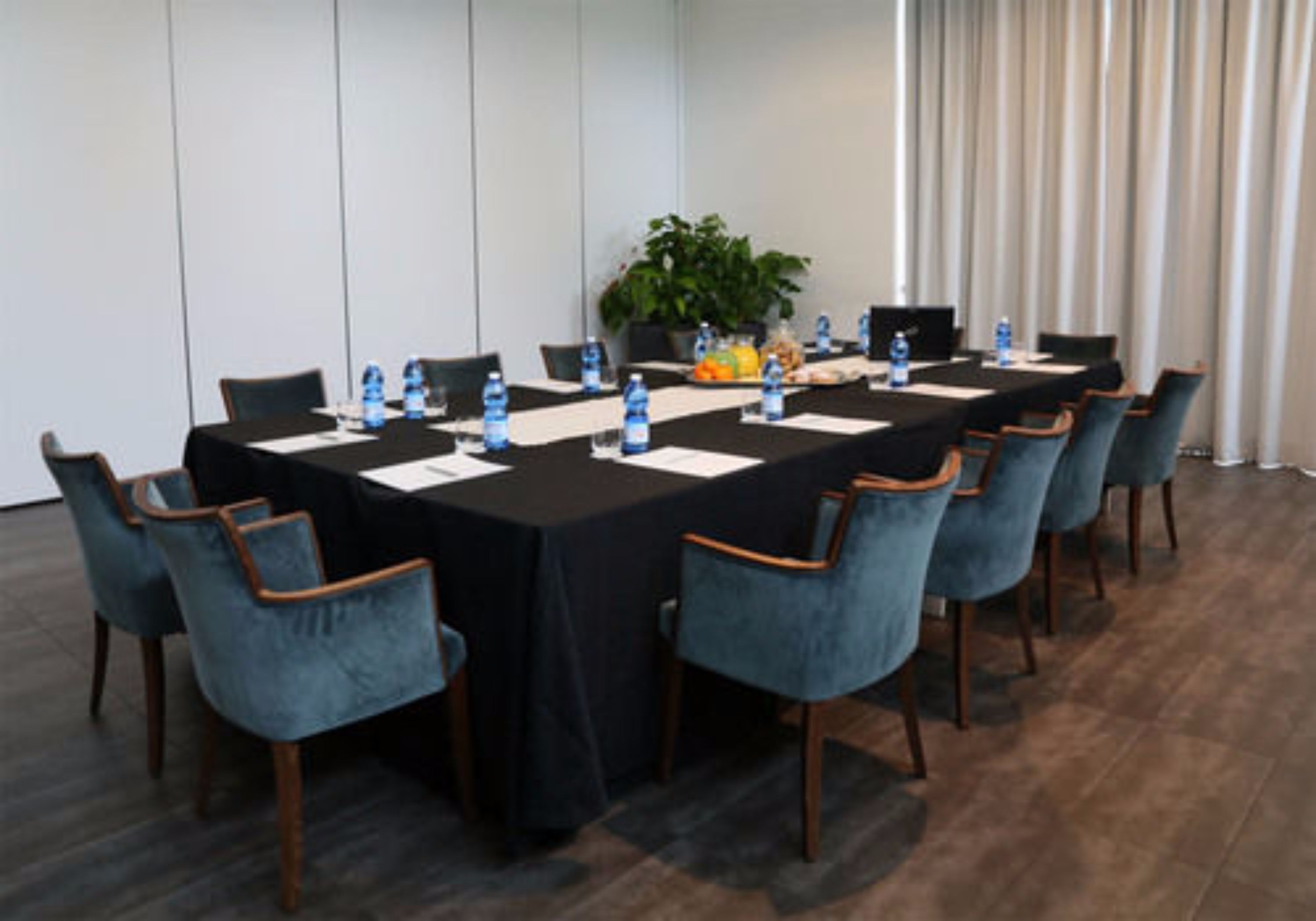 A conference room with a long table, blue chairs, water bottles, and a plant on the table.