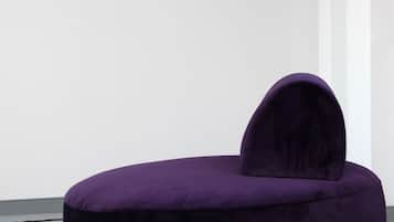 A purple, round, velvet chair with a unique backrest design against a plain wall.