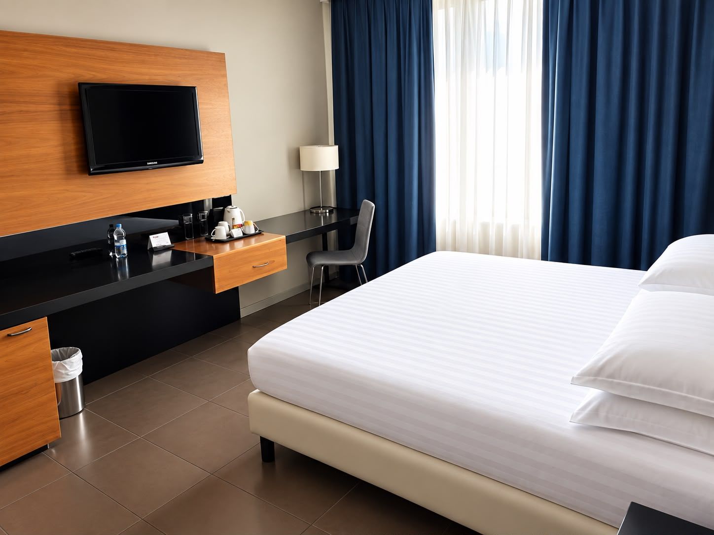 Habitación de hotel con cama, escritorio con televisor de pantalla plana, silla y ventana con cortinas.