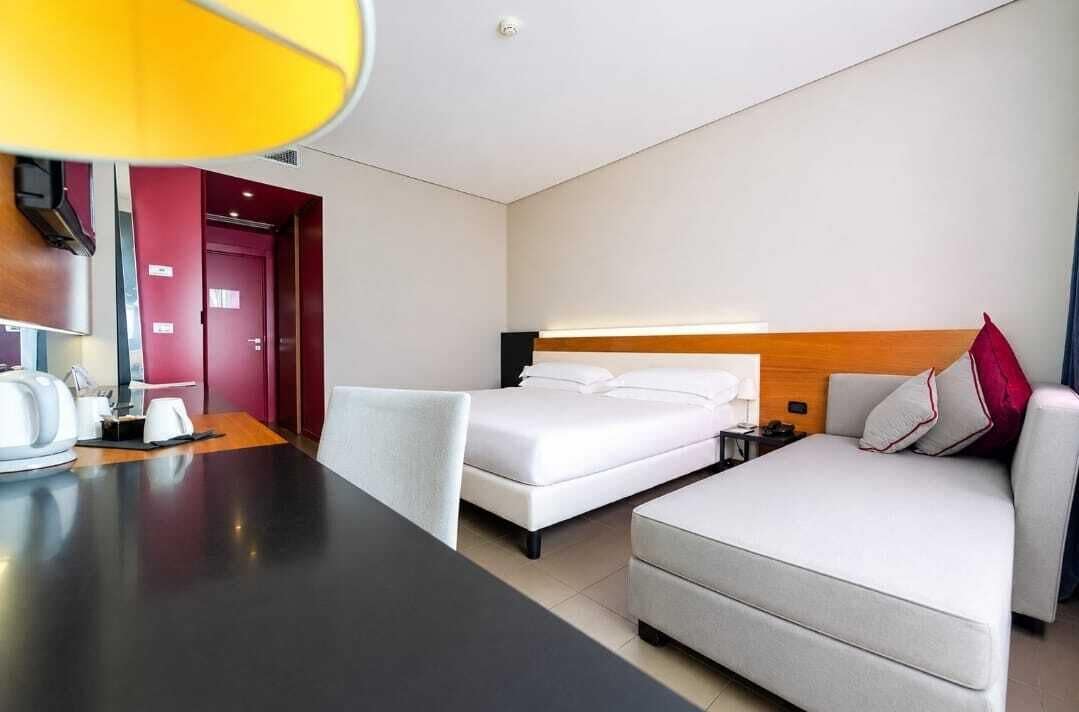 A hotel room with a bed, a sofa, a desk, and a lamp.