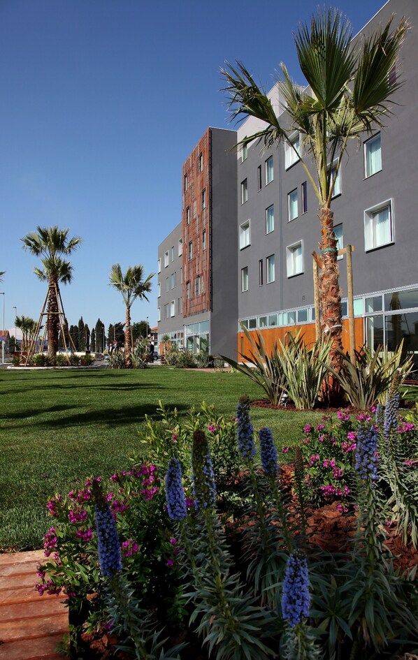 A modern building with multiple windows and a well-maintained lawn with various plants and flowers. - Cosmopolitan Hotel (Civitanova Marche)