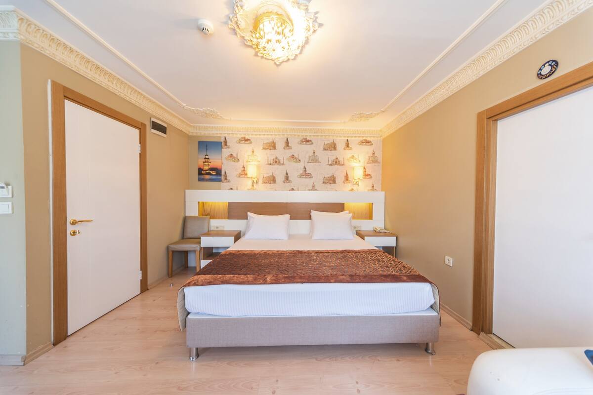 A hotel room with a large bed, a nightstand, a chair, and a wall with a patterned design.