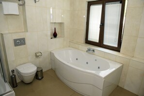 A bathroom with a white bathtub, toilet, and a window with blinds. - Taya Hatun Hotel (Istanbul)