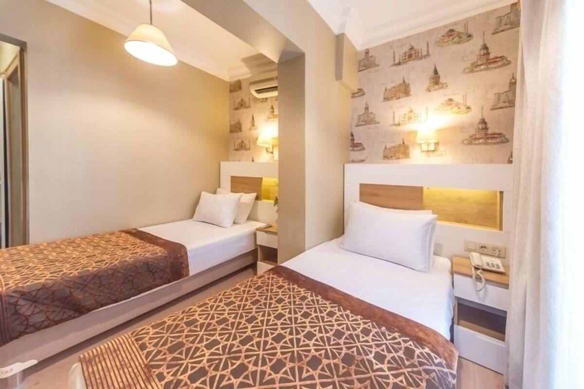 A hotel room with two beds, a patterned rug, and a wall with cityscape wallpaper.