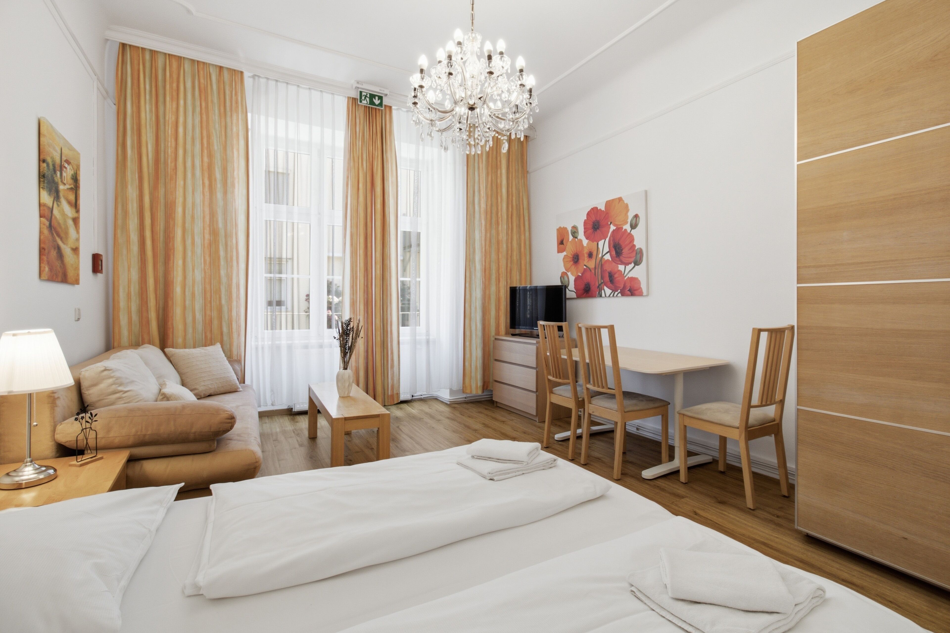 A hotel room with a bed, a desk, a chair, a TV, and a chandelier.