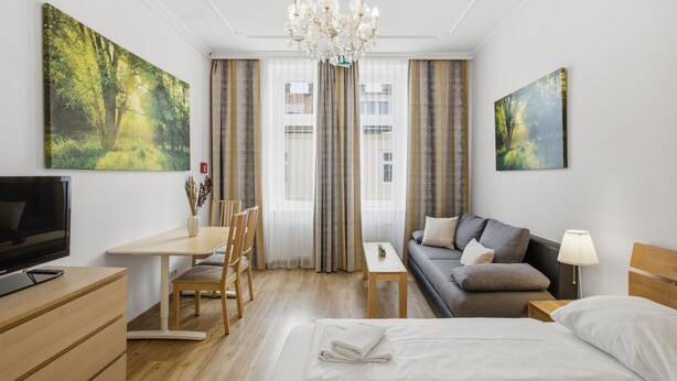 A hotel room with a bed, a desk, a sofa, a TV, and two paintings. - AJO Vienna Messe - Contactless Check-in (Vienna)