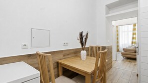 A modern kitchen with white cabinets, a wooden dining table, and chairs. There is a vase with dried plants on the table. - AJO Vienna Messe - Contactless Check-in (Vienna)