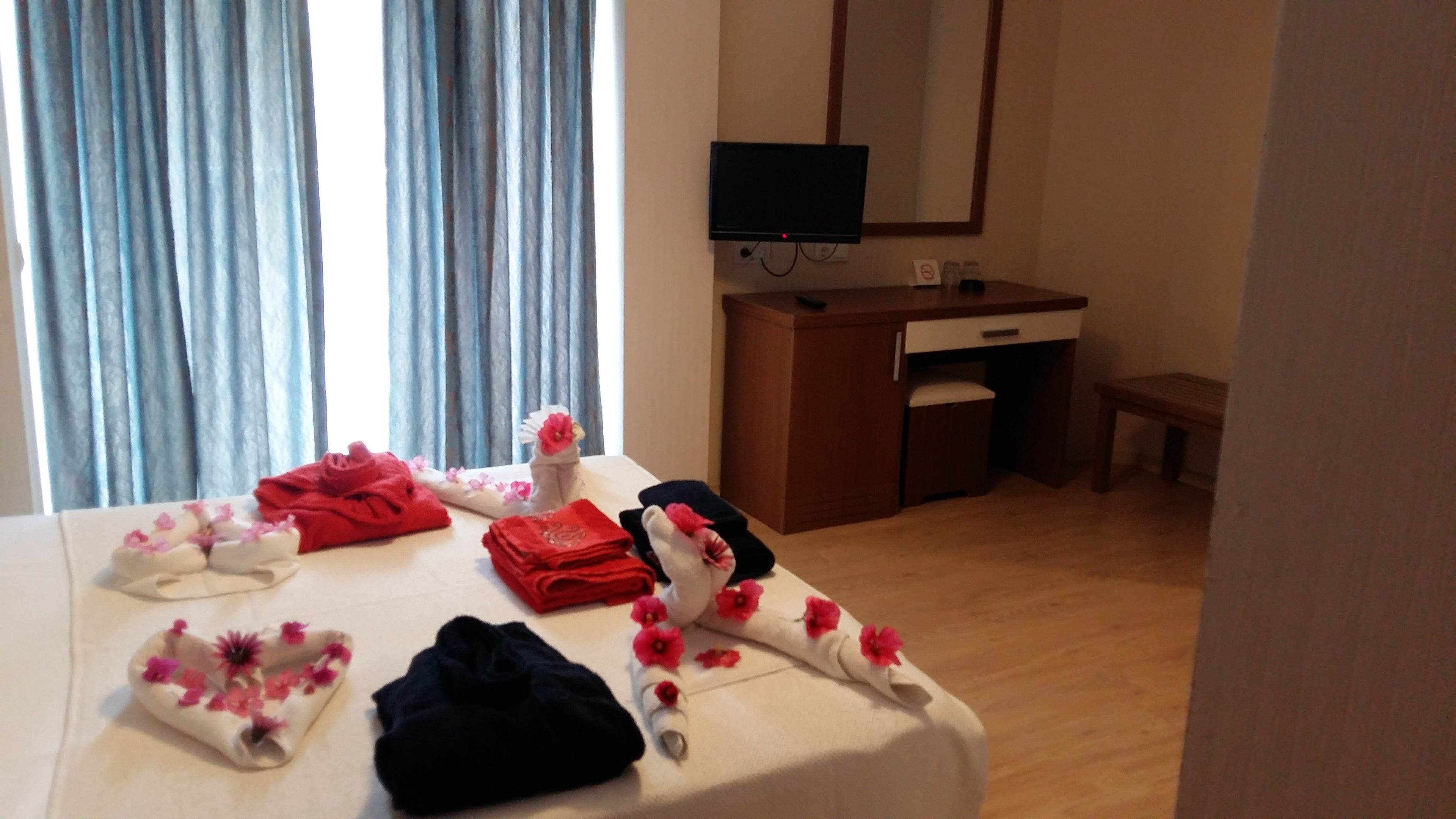 A hotel room with a bed, a desk, a television, and a window with curtains.