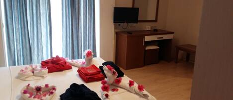 A hotel room with a bed, a desk, a television, and a window with curtains.