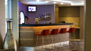 A bar area with a wooden counter, red bar stools, a television mounted on the wall, and a shelf with bottles. - Supreme Marmaris Hotel (Marmaris)