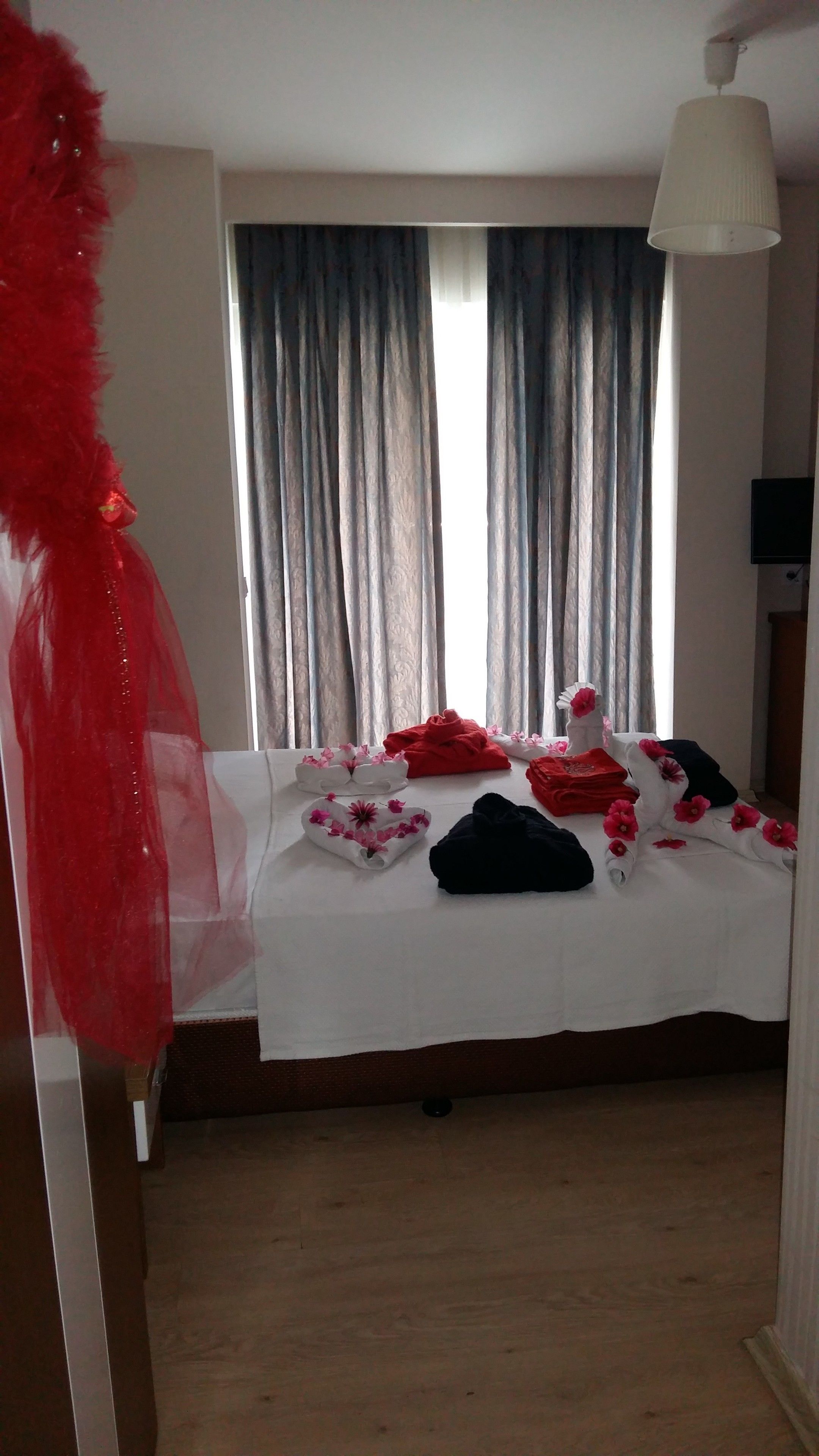 A hotel room with a bed, a window with curtains, a lamp, and a television.