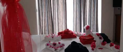 A hotel room with a bed, a window with curtains, a lamp, and a television.