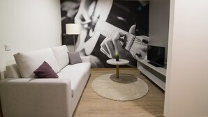 A modern living room with a white sofa, a small round table with a lamp, and a large wall mural of a guitar player. - Porto Coliseum Hotel (Porto)