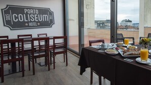 A dining area with a table set for breakfast, a sign reading "Porto Coliseum Hotel", and a view of the city through large windows. - Porto Coliseum Hotel (Porto)