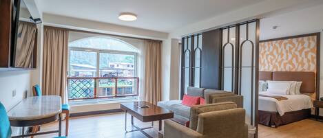 A hotel room with a balcony, a sofa, a bed, and a dining area with a table and chairs.