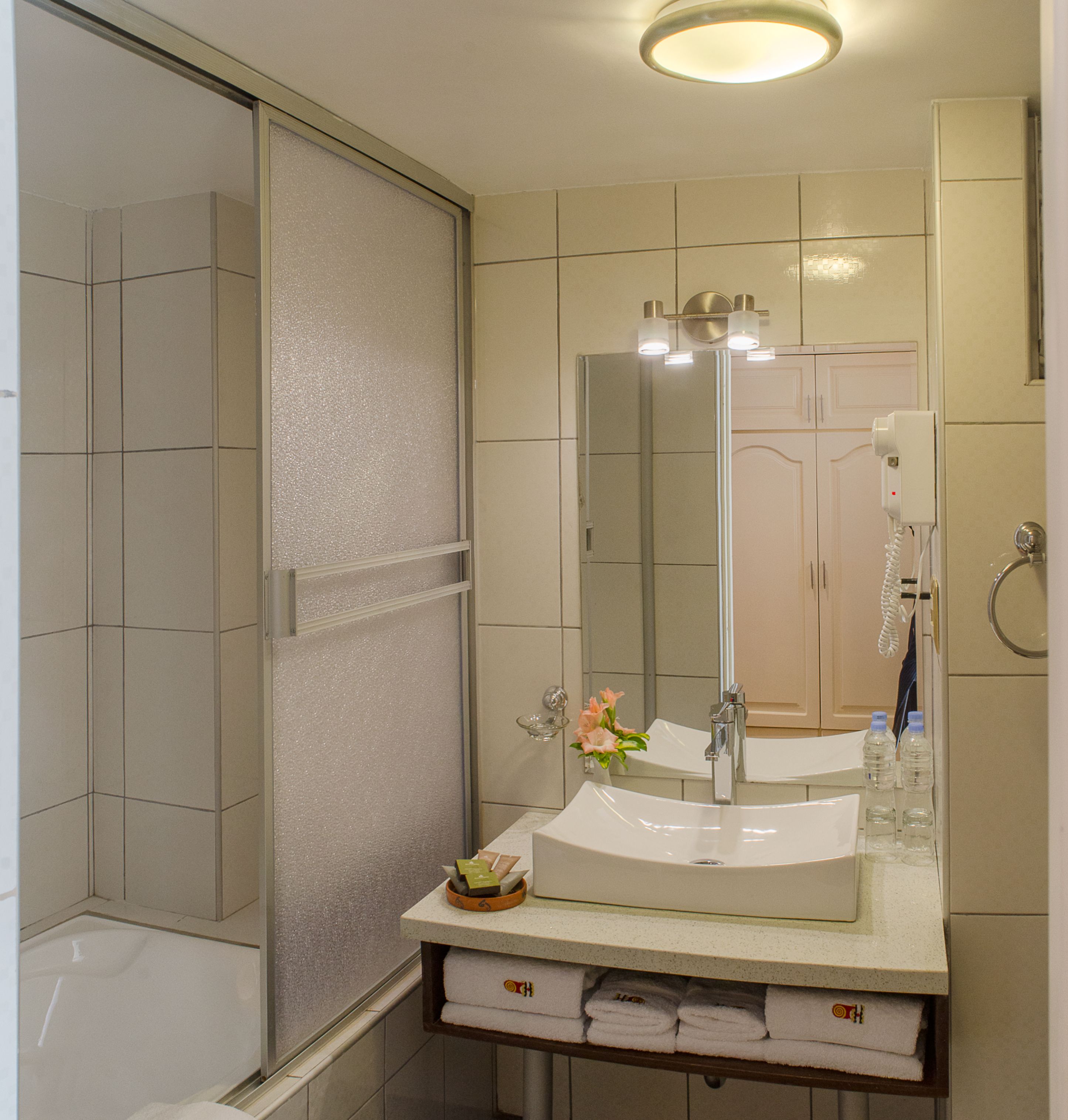 A bathroom with a glass shower enclosure, a sink with a mirror, and a towel rack with folded towels.