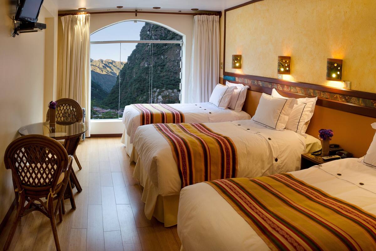 Una habitación de hotel con dos camas, una mesa de comedor y vistas a las montañas.
