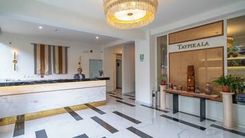 A hotel reception area with a marble counter, a chandelier, a reception desk, and a wall with the name 'Taypikale'.