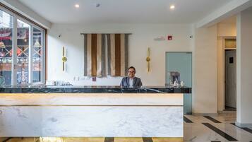 A reception desk with a marble counter, a person standing behind it, and a striped curtain in the background.